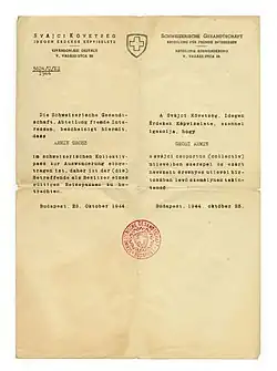 Photographie d'une lettre au papier jauni, portant un entête (préimprimé) et un corps de texte (tapé à la machine à écrire) en allemand et en hongrois, doté d'un tampon rouge au centre.