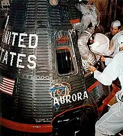 Plusieurs personnes en aident une autre à passer la porte exigüe d'un vaisseau spatial.