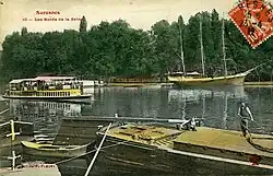 Photographie d'un fleuve avec plusieurs bateaux et une forêt en arrière-plan.