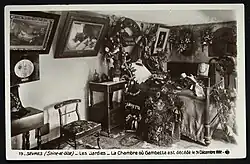 Carte postale ancienne montrant une chambre ornée de nombreux tableaux, couronnes de fleurs et objets d'art.