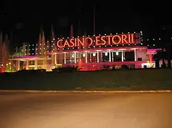 Photographie nocturne montrant un bâtiment alongé, où Casino Estoril est écrit en lettres rouges illuminées,