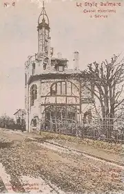 Carte postale colorisée montrant un bâtiment assez compact surmonté d'une très étroite tourelle avec clocheton