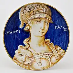 Plat peint en bicolore bleu et ocre à buste féminin orné d'une armure et d'un casque à plumes ; sur le fond bleu le mot « Marfisa » ; typologie des « Belles Femmes », Casteldurante, première moitié du XVIe&nbsp;siècle.