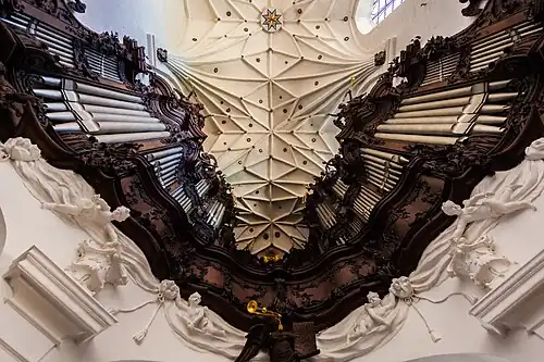 Photographie en contre-plongée d'un orgue en fer à cheval surmonté d'une voûte blanche à nervures décorée d'étoiles.