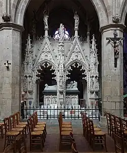 Photo représentant un tombeau monumental néogothique en pierre blanche, dans un bas-côté d'église.