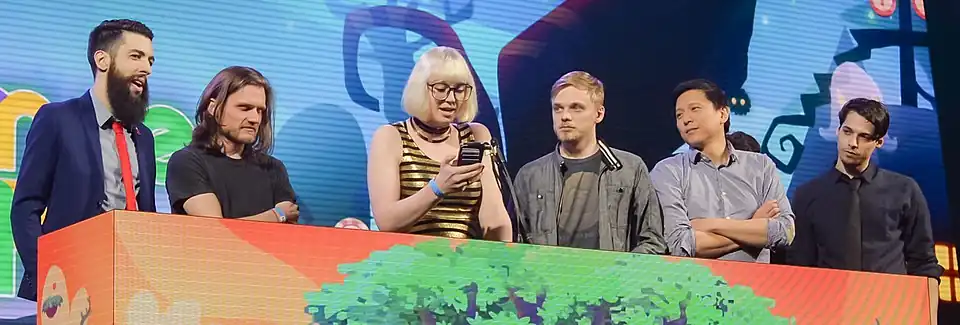 Six personnes derrière une tribune, une femme au centre lit sur son téléphone.