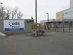 Photo de l'accès de la centrale. Une bannière EDS est affichée sur la clôture en treillis métalalique.