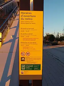 Panneau jaune en français, anglais et breton avec les horaires de fonctionnement du métro et diverses informations relative à la vidéosurveillance, aux défibrillateurs ou encore à l'interdiction de fumer et de vapoter.