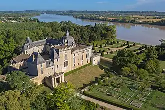 Photo aérienne d'un grand château rectangulaire, avec une cour intérieure, aux murs de pierre blonde et aux toits d'ardoise, entouré de jardins. À l'arrière-plan un grand cours d'eau