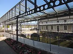 Photographie présentant un déambulatoire quadrangulaire dallé recouvert d'une structure métallique légère supportant une verrière.