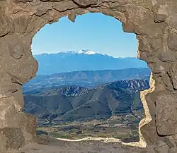 Derrière une voute, une série de vallées et montagnes, un mont neigeux à l'horizon.