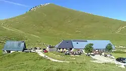 Deux bâtiments aux toits en taule bleutée sous un sommet couvert d'alpages.