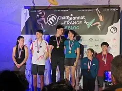 photo d’un podium sur lequel se tiennent les médaillés hommes et femmes, souriants, avec leurs médailles autour du cou et des bouquets de fleurs à la main