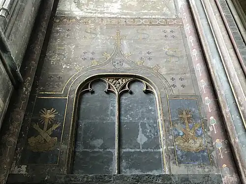 Mur de pierre peint. En haut, les lettres F et S sont entrelacées. En bas, de part et d'autre d'une niche vide, sont peints deux bras croisés devant une croix.