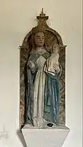photo en couleurs de la statue de la Vierge à l'Enfant sur un socle blanc fixé au mur.