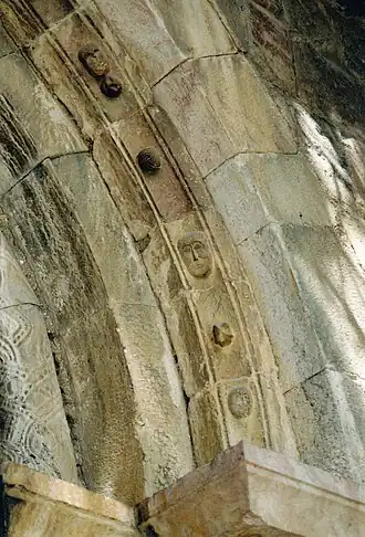 Voussure du portail ornée de boules, de masques humains et de personnages fantastiques.