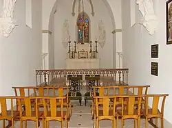 Intérieur de la chapelle, bancs d'église, prie-dieu, vitraux autel et chandeliers liturgiques.