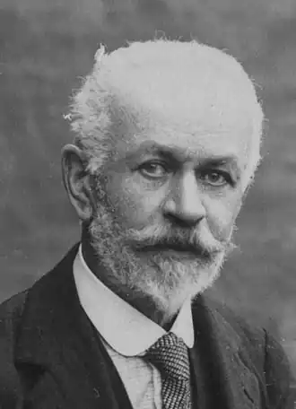 Photo noir et blanc d'un homme âgé, au crane partiellement dégarni et aux cheveux et barbe blanc.