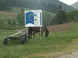 photographie couleurs : charrette à cheval derrière un panneau au logo européen