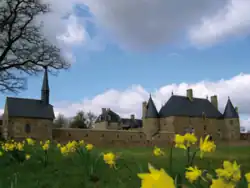 Photographie d'un manoir, à droite, et de sa chapelle, à gauche, aperçus depuis un tapis de jonquilles.