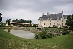 Photographie du château avec sa douve au premier plan et ses communs à gauche.