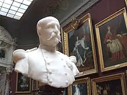 Buste en marbre blanc du duc, âgé, en tenue de militaire avec les tableaux de la grande galerie en arrière plan
