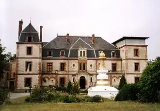 photo couleur d'un château de style XVIIIe&nbsp;siècle à toit en ardoise. Au premier plan, un stoupa orne le parc.