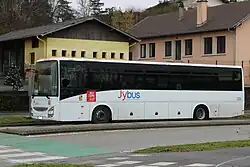 Photographie en couleurs d’un autocar blanc et noir stationné devant des bâtiment scolaires à Chavanod.