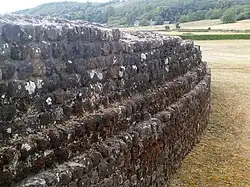 Photographie en couleurs d'un mur courbe dont les assises en retraits successifs dessinent des ressauts.