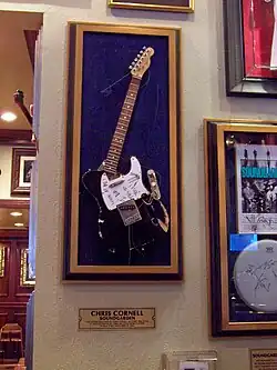 Photographie d'une guitare cassée exposée dans une vitrine.