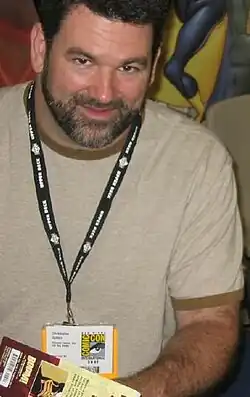 Un homme brun barbu souriant.