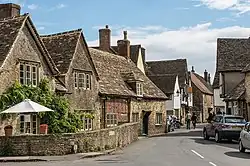 Petites maisons en pierres de couleur gris foncé séparées de la route goudronnée par un muret en pierres de la même couleur.