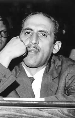 Image en noir et blanc du visage d'un homme appuyé sur son poing droit, regardant le spectateur.