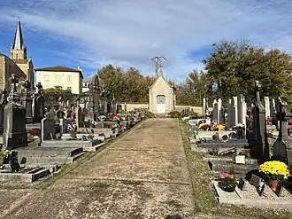 Une allée de cimetière bordée de tombes qui se termine sur une chapelle funéraire.
