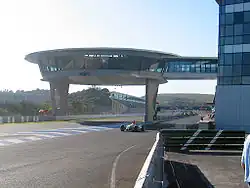 Photo d'une ligne droite de circuit, surmontée d'une arche en béton et en verre