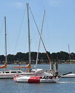 Voilier blanc et rouge progressant au moteur dans un bassin, entre les pontons.