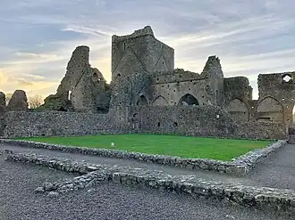 Photographie d'un cloître monastique dont il ne reste que les fondations. L'église mieux conservée est au second plan.