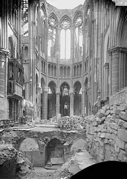 Photographie en noir et blanc. Vue sur le chœur avec ses voûtes effondrées et sans verrière. Nombreux gravats au sol. La crypte est à ciel ouvert.