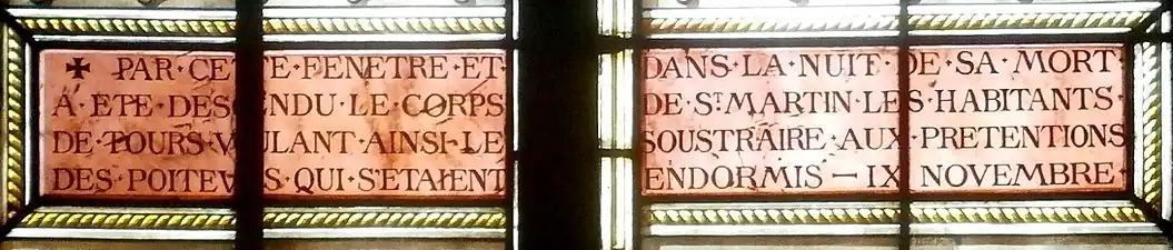 Photographie en couleurs d'un cartouche de vitrail mentionnant un évènement hagiographique.