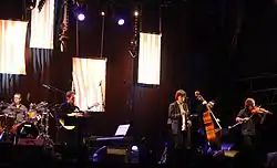 Denez Prigent&nbsp;chantant sur scène accompagné de ses musiciens.