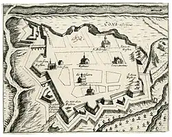 Gravure noir et blanc. Vue cavalière d'une ville entièrement ceinte de remparts. Les principaux édifices sont représentés, ainsi que les batteries de canons, les reliefs, les voies et les cours d'eau, dont le Gesso.