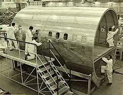 Cliché noir et blanc. Section d'un cylindre divisé en deux vu de trois quarts. Trois hommes à l'extérieur sur un échafaudage. Deux hommes vers l'avant. Tous en blanc.