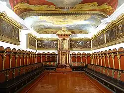 La maison du chapitre entourée de stalles avec une tribune centrale surmontée d'un groupe sculpté en bois représentant Jean Duns Scot avec l'Immaculée Conception, patronne des Franciscains.