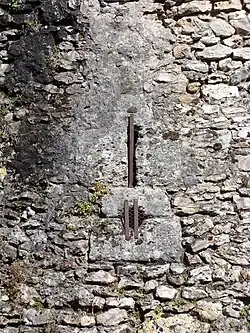 Photographie en couleurs d'un trou circulaire surmonté d'une fente verticale dans un mur en maçonnerie.