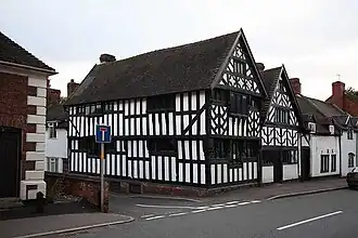 Photo d'une maison aux murs blancs avec des poutres en bois apparentes, située à un carrefour