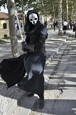 Homme habillé en noir avec un masque blanc.