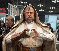 Homme barbu aux habits beige et blancs et avec une capuche