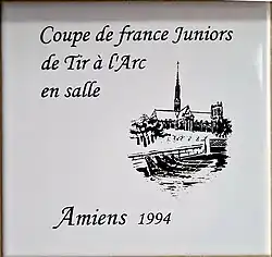 Photo d'un carreau de faïence avec un dessin au trait de la cathédrale d'Amiens, avec l'inscription coupe de France juniors de tir à l'arc en salle, Amiens 1994.