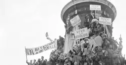 Photographie en noir et blanc de manifestants en haut d'une tour tenant des banderoles sur lesquelles on peut lire « Vive la République » et « Non au fascisme de De Gaulle ».