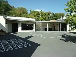 Photographie en couleurs de bâtiments modernes au fond d'une cour sur le sol de laquelle des jeux sont dessinés.